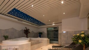 Een wellnessruimte met een jacuzzi, massagestoelen en een plafond met sterrenlichtdesign.
