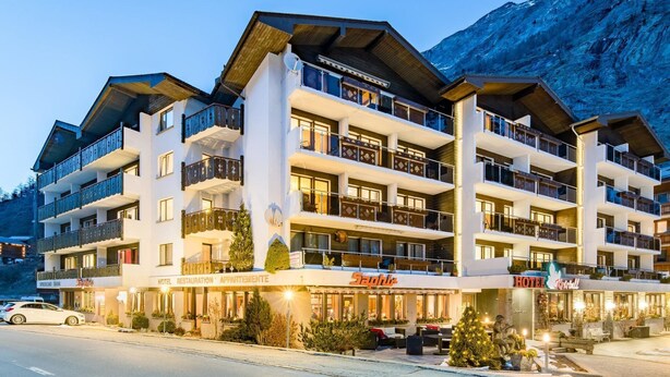 Een hotel met meerdere verdiepingen, met balkons, een restaurant en een bord van een skigebied.