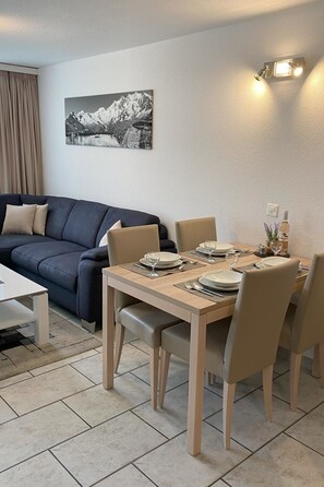 A dining area with a table set for four, a sofa, and a wall-mounted light fixture. - Apartments Arcadia Appartement/Fewo 4-Bettwohnung Mittelgrat by Interhome (Saas-Grund)