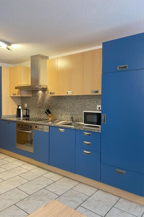 Eine moderne Küche mit blauen Schränken, einer Edelstahl-Dunstabzugshaube, einer Mikrowelle und einem Einbauofen.