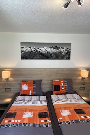 A hotel room with two beds, a large mountain landscape painting above, and wall-mounted lamps on either side. - Apartments Arcadia Appartement/Fewo 4-Bettwohnung Mittelgrat by Interhome (Saas-Grund)