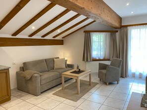 Ein Wohnzimmer mit einer Couch, einem Sessel, einem Couchtisch und einem Fenster mit Vorhängen.