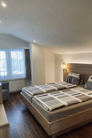 Ein Hotelzimmer mit einem großen Bett, einem Nachttisch, einem Sessel und einem Fenster mit Vorhängen.