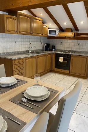 A kitchen with wooden cabinets, a microwave, a coffee maker, and a dining table set for two with plates, cutlery, and a wine glass. - Apartments Arcadia Appartement/Fewo 4-Bettwohnung Weissmies by Interhome (Saas-Grund)