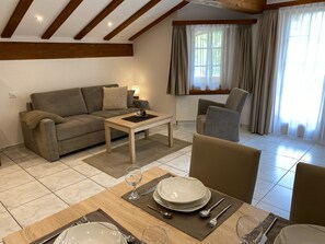 A living room with a sofa, a coffee table, and a dining area set with plates, glasses, and cutlery. - Apartments Arcadia Appartement/Fewo 4-Bettwohnung Weissmies by Interhome (Saas-Grund)