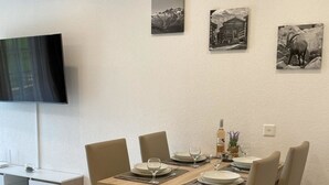 Ruokailutilassa on puinen pöytä, jonka ääreen on katettu neljälle, ja pöydän ympärillä on tuoleja. Seinälle on asennettu televisio, joka sijaitsee pöydän yläpuolella.
