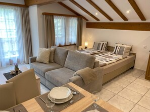 A modern bedroom with a sofa, a bed with striped bedding, and a dining area with a table set for two. - Apartments Arcadia Appartement/Fewo 4-Bettwohnung Dom by Interhome (Saas-Grund)