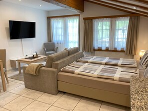 Ein modernes Wohnzimmer mit einer Couch, einem Fernseher, einem Esstisch und einem Sessel.