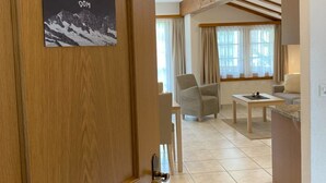 Habitación de hotel con puerta de madera, zona de comedor con mesa y sillas, y vistas a las montañas.
