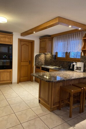 A kitchen with wooden cabinets, a granite countertop, a built-in oven, and a window with a view. - Apartments Arcadia Appartement/Fewo 6-Bettwohnung Allalin by Interhome (Saas-Grund)