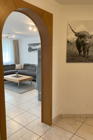 Un salon moderne avec un canapé gris, une table basse en bois et un grand tableau représentant un yak.