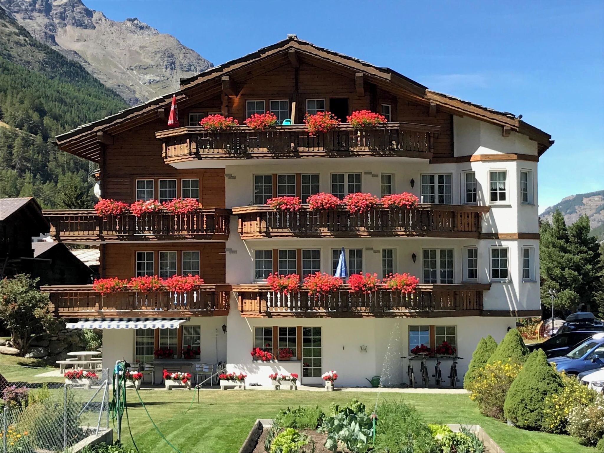 Un hotel de varios pisos con balcones decorados con flores, un jardín y montañas al fondo.