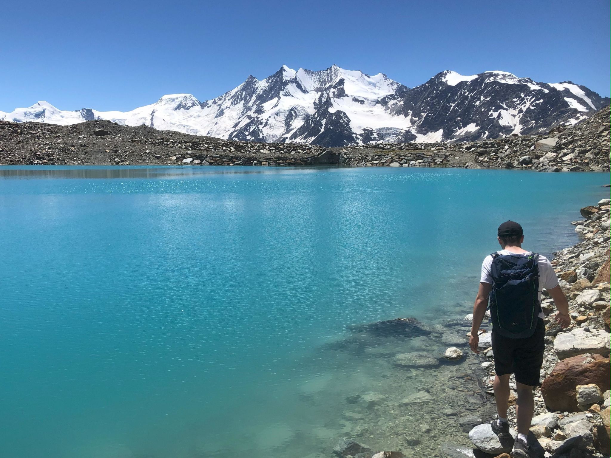 Una persona in piedi accanto a un lago cristallino con montagne sullo sfondo.