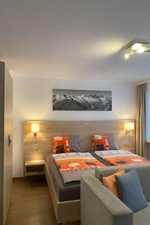 Ein Hotelzimmer mit zwei Betten, einer Schlafcouch, einem Wandbild und Nachttischlampen.