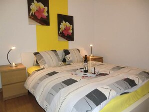 Ein Schlafzimmer mit einem Bett, zwei Nachttischlampen, einem Nachttisch und einer Wand mit zwei Blumenbildern.