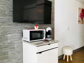 Een kleine keuken met een magnetron, koffiezetapparaat en een klein krukje.