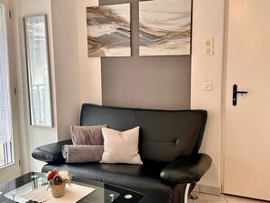 Ein modernes Wohnzimmer mit einer schwarzen Ledersofa, einem Glastisch und einem an der Wand befestigten abstrakten Kunstwerk.