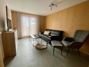 Ett vardagsrum med en soffa, en fåtölj, ett soffbord och en tv som står på ett TV-bord.
