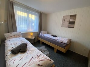 Ein Hotelzimmer mit zwei Betten, einem fensterbelaubten Fenster, einer Nachttischlampe und einem Wandbild.