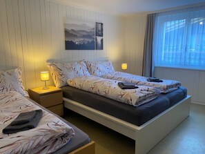 A double bed with a floral bedspread, two bedside lamps, a nightstand, and a window with curtains. - casa genepy Appartement/Fewo 6-Bettwohnung by Interhome (Saas-Grund)