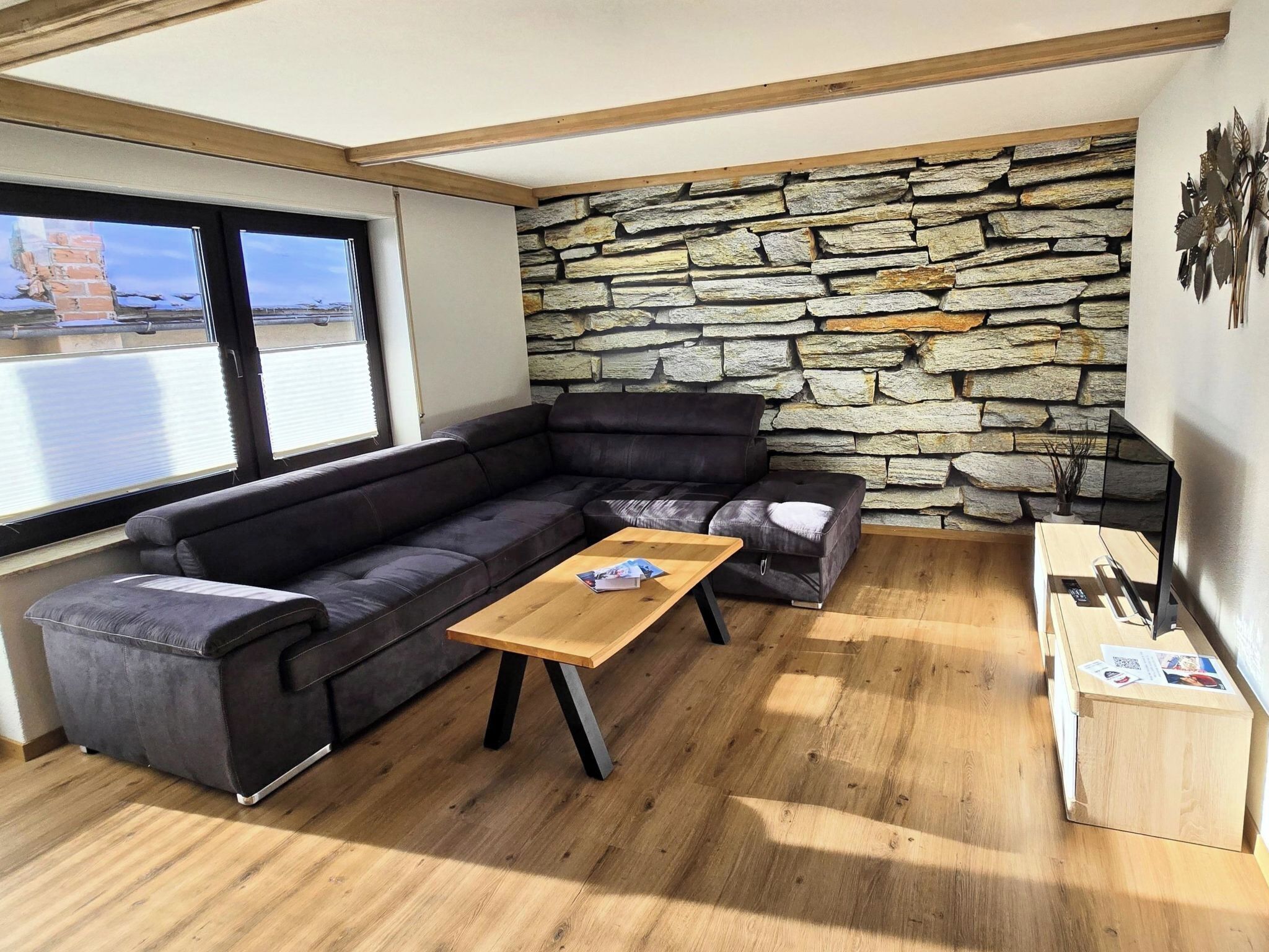 Ein modernes Wohnzimmer mit einer Steinwand, einem schwarzen Ledersofa, einem Holztisch und einem TV-Schrank.