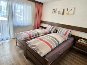 Ein Doppelbett mit gestreifter Bettwäsche, ein hölzerner Kopfteil, ein Nachttisch mit Lampe und ein Fenster mit durchsichtigen Vorhängen.