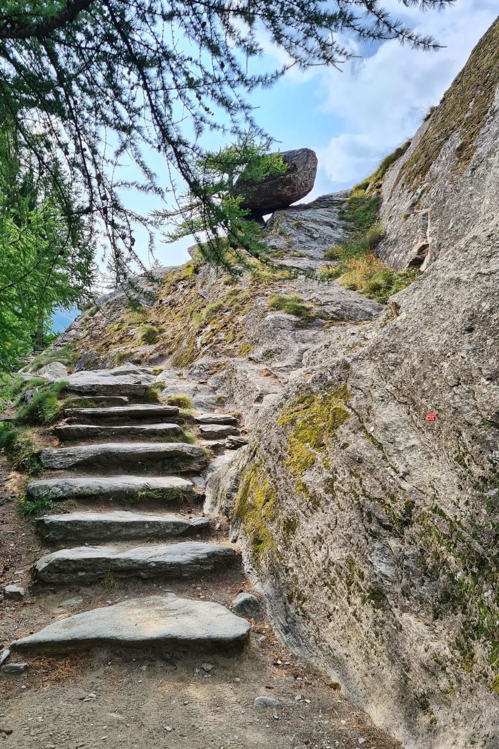 Eine steile Steintreppe führt einen einen felsigen Hang hinauf, spärliche Vegetation und ein klarer Himmel.