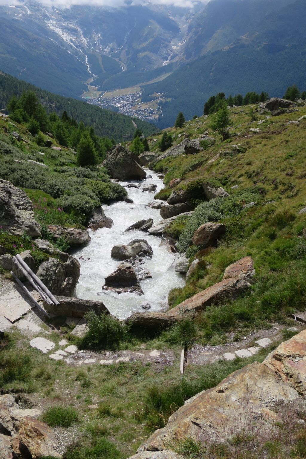 Un paysage montagneux, avec une rivière sinueuse, un terrain rocheux et un village situé au loin.