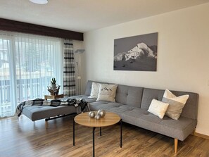 A modern living room with a grey sofa, a round coffee table, and a mountain landscape painting on the wall. - Ferienhaus Alea Appartement/Fewo 4-Bettwohnung Nr. 20 by Interhome (Saas-Grund)