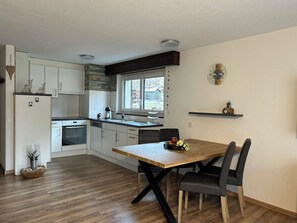 A modern kitchen with white cabinets, a wooden dining table, and a window with a view of buildings. - Ferienhaus Alea Appartement/Fewo 4-Bettwohnung Nr. 20 by Interhome (Saas-Grund)