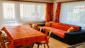 Ein Essbereich mit Tisch und Stühlen, einer Couch und einem Fenster mit Vorhängen.