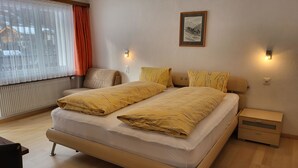 Ein Hotelzimmer mit Bett, Nachttischen, einem Sessel, einem Heizkörper und einem Fenster mit Vorhängen.