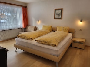 Een hotelkamer met een bed, nachtkastjes, een stoel, een radiator en een raam met gordijnen.
