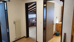 Een kamer met een houten vloer, een radiator, een deur naar een andere kamer en een kleine prullenbak.