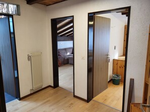 Ein Zimmer mit Holzboden, Heizkörper, einer Tür zu einem anderen Raum und einer kleinen Mülltonne.