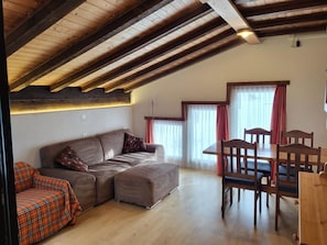 Ein Loft-Wohnraum mit Holzbalkendecke, einer Couch, einem Esstisch mit Stühlen und einem fenster mit Vorhängen.