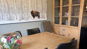 Un comedor con mesa de madera, sillas negras, un florero de vidrio con flores y un mueble con puertas de cristal.