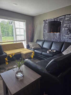 A living room with a sofa, a coffee table with a vase of flowers, and a cityscape wall art.
