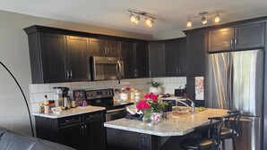 Una cocina moderna con armarios oscuros, electrodomésticos de acero inoxidable y una isla central con taburetes de bar.
