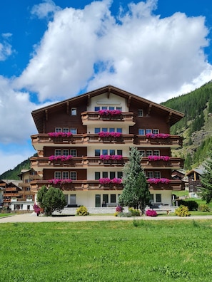 Ein mehrstöckiges Hotel mit Balkonen, die mit Blumen geschmückt sind, vor einer Berglandschaft.
