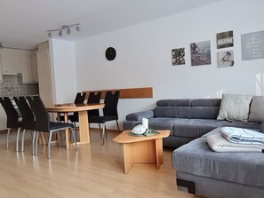 Ein modernes Wohnzimmer mit einem grauen Sofa, einem Holztisch und einem Essbereich mit einem Holztisch und schwarzen Stühlen.