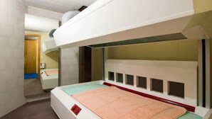 Una stanza con un letto a castello, una scrivania piccola e una porta che dà su un'altra stanza.