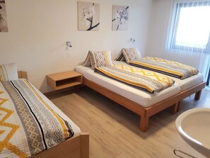 Ein Doppelzimmer mit zwei Betten, einem Nachttisch, einer kleinen Holzkabine und einem Badezimmer mit einem runden Waschbecken.