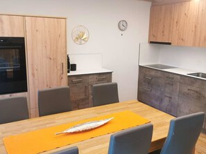 A modern kitchen with wooden cabinets, a white countertop, and a dining table with chairs. - Ferienhaus Adonis Appartement/Fewo 5-Bettwohnung "Fletschhorn" by Interhome (Saas-Grund)