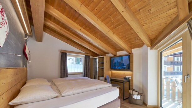 Une chambre avec un plafond en bois, un lit, un bureau, une télévision et une fenêtre donnant sur un beau paysage.