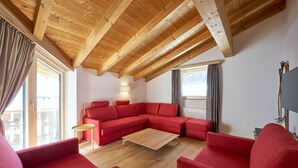 Un salon moderne avec un plafond en bois, un canapé d’angle rouge et une table basse en bois.