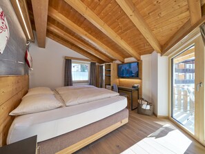 Ein Schlafzimmer mit einem großen Bett, Holzbalken an der Decke, einem Fernseher und Blick ins Freie.