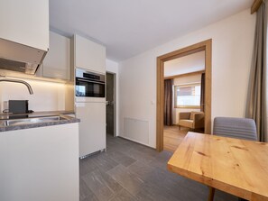 A compact kitchen with modern appliances, a dining area with a wooden table, and a view through an open doorway. - Apartments Chesa Grischuna, (Samnaun-Dorf) by Interhome (Samnaun)