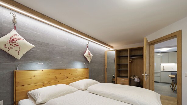 Een slaapkamer met een houten hoofdbord, twee bedden, een kledingkast en een kleine kitchenette.