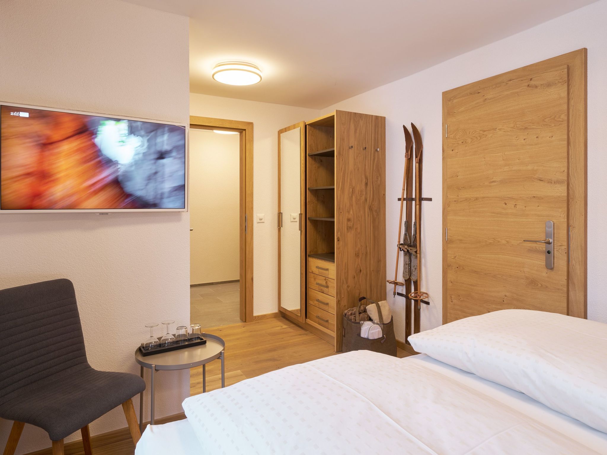 A hotel room with a bed, a chair, a TV, a wooden wardrobe, and skis.
